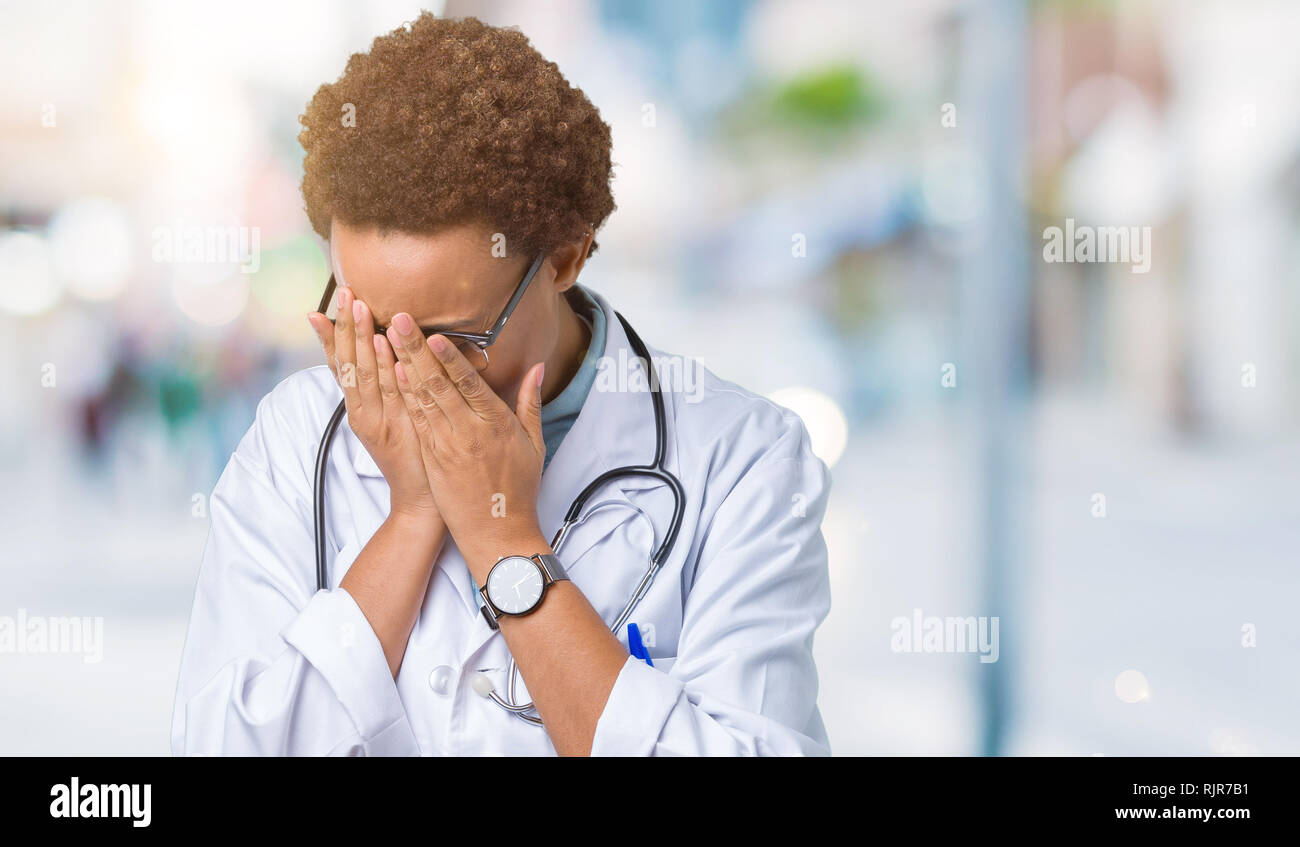 Young african american doctor woman wearing medical coat over isolated background with sad expression covering face with hands while crying. Depressio Stock Photo