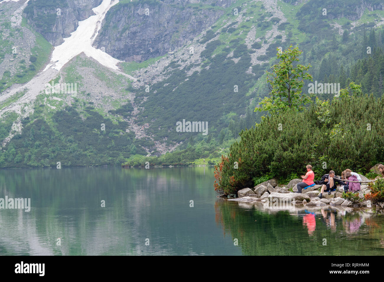 Visitors relax on rocky banks of  Morskie Oko lake (Eye of the Sea) in the Tatra Mountains in the Tatra National Park,Lesser Poland Voivodeship, Polan Stock Photo