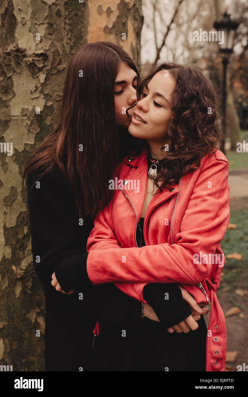 Long Haired Man Hugging And Kissing Woman Near Tree Stock Photo