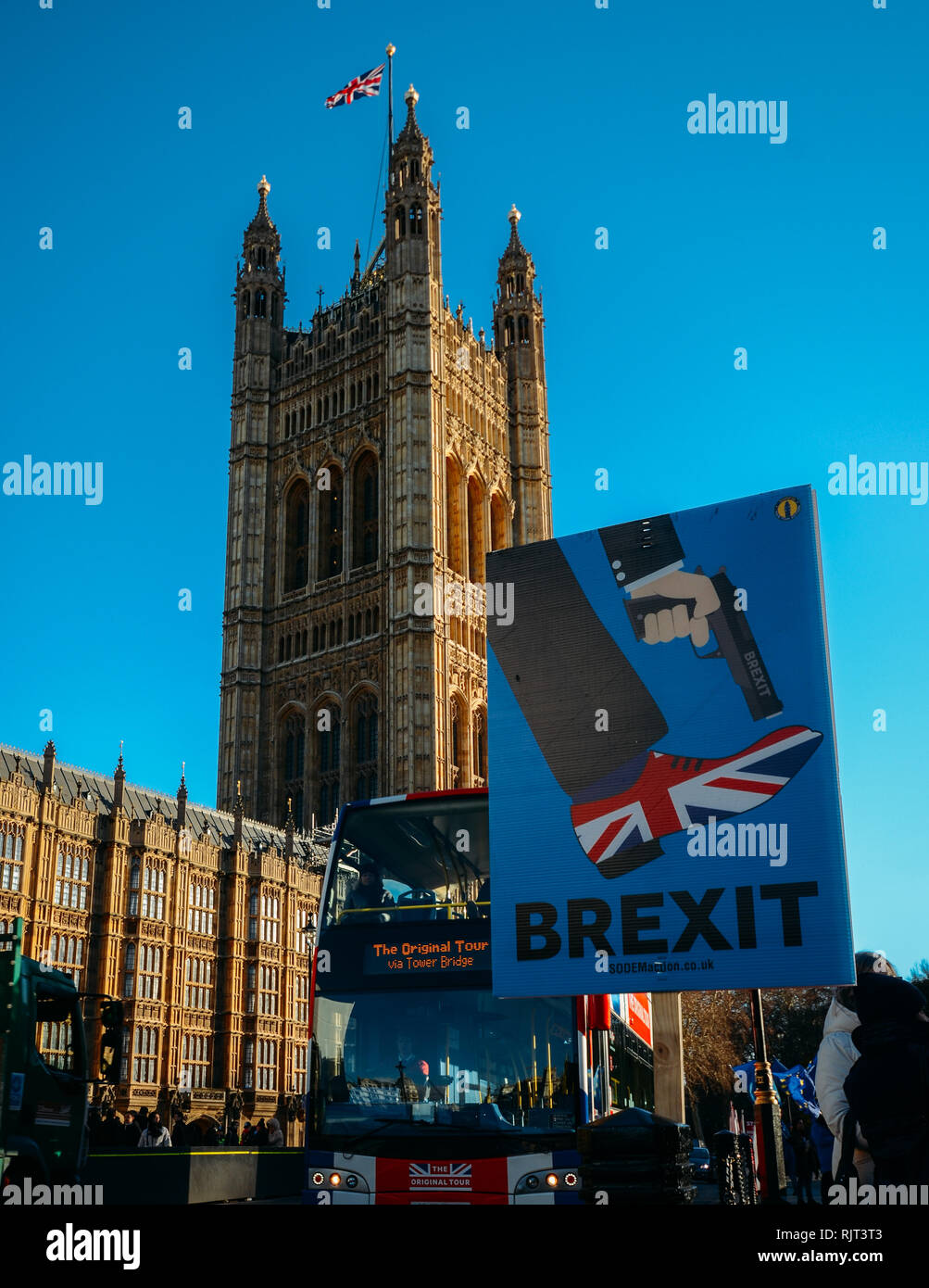 London, UK - Feb 7, 2019: Anti-Brexit placard outside, Westminster, London, UK depicting Brexit as shooting the UK in the foot with double-decker bus painted with Union Jack colours in background Credit: Alexandre Rotenberg/Alamy Live News Stock Photo