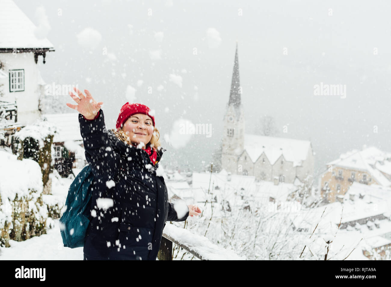 Woman in red hat having a snowball fight in Hallstatt old town during snow storm, Austria Stock Photo