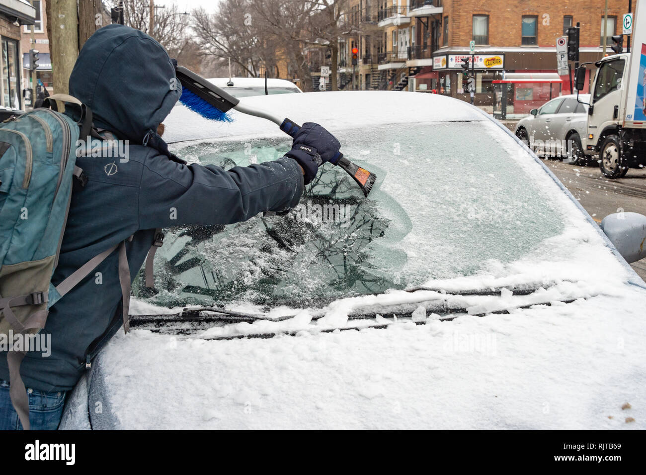 Montreal, Canada - 7 February 2019: man cleaning car windshield from ice with scraper tool. Stock Photo