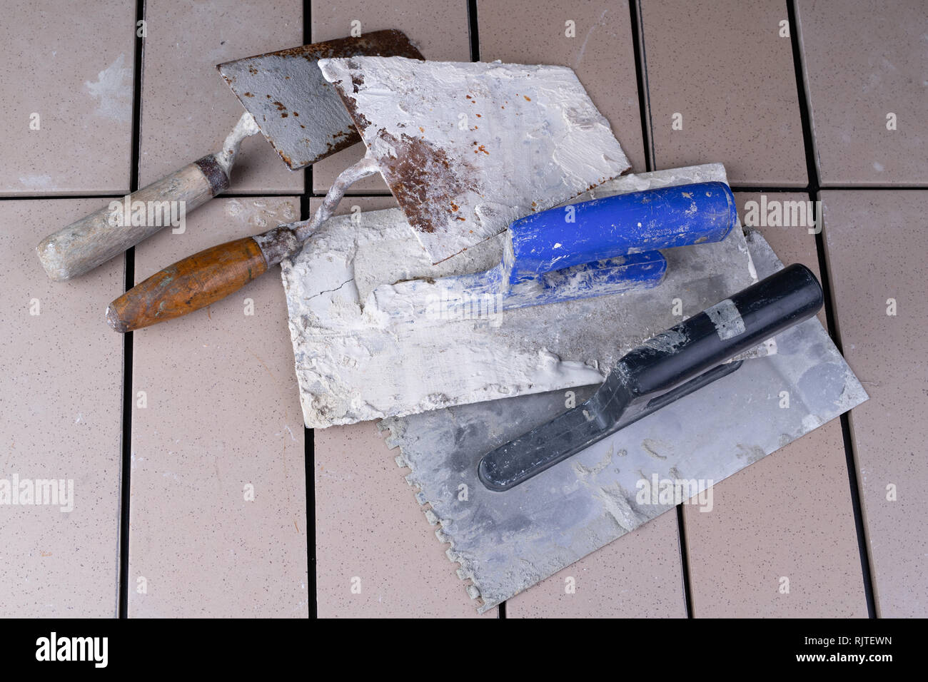 Tiles cut to size and trowels for applying mortar. Masonry accessories on a workshop table. Dark background. Stock Photo