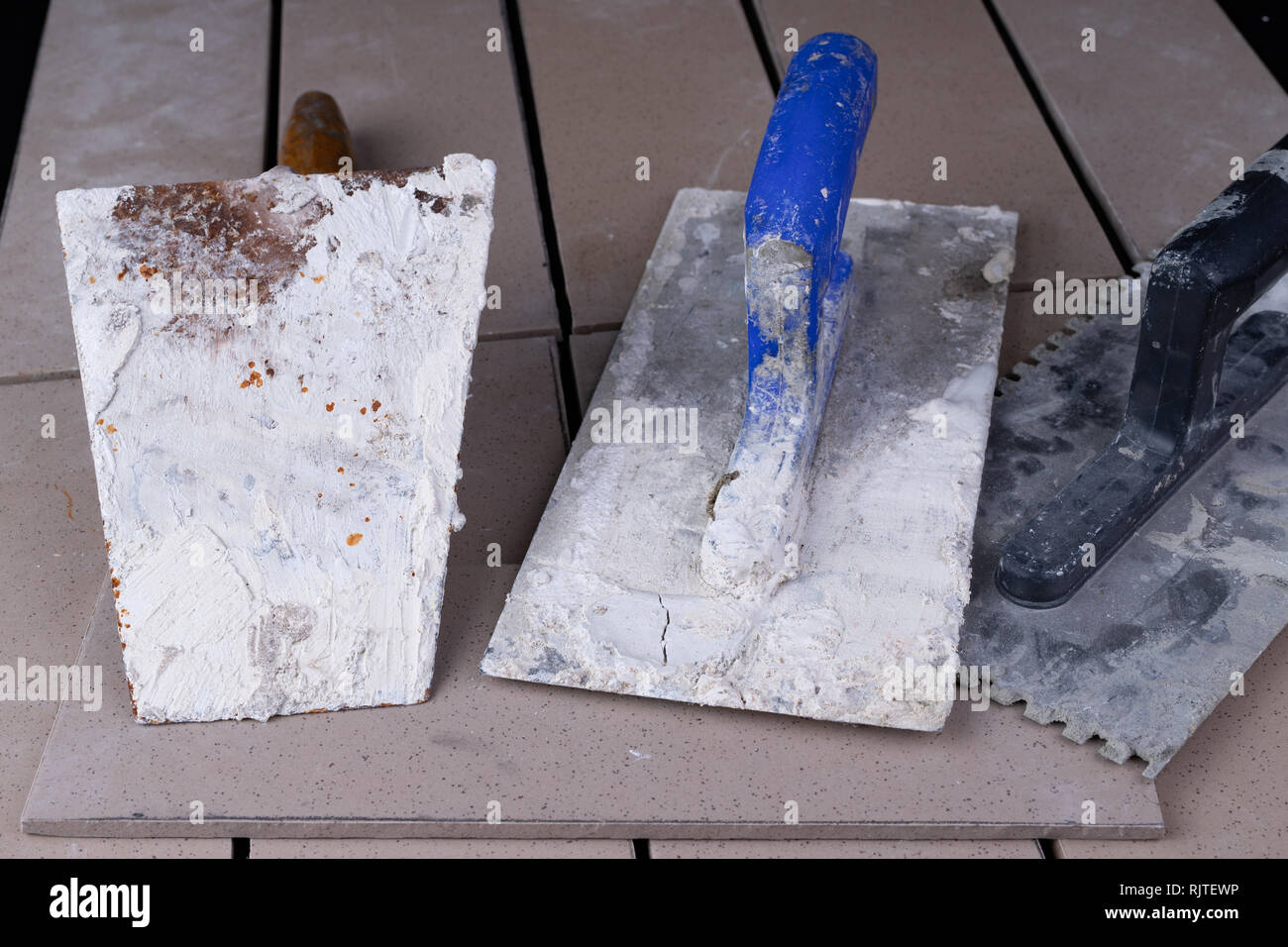 Tiles cut to size and trowels for applying mortar. Masonry accessories on a workshop table. Dark background. Stock Photo