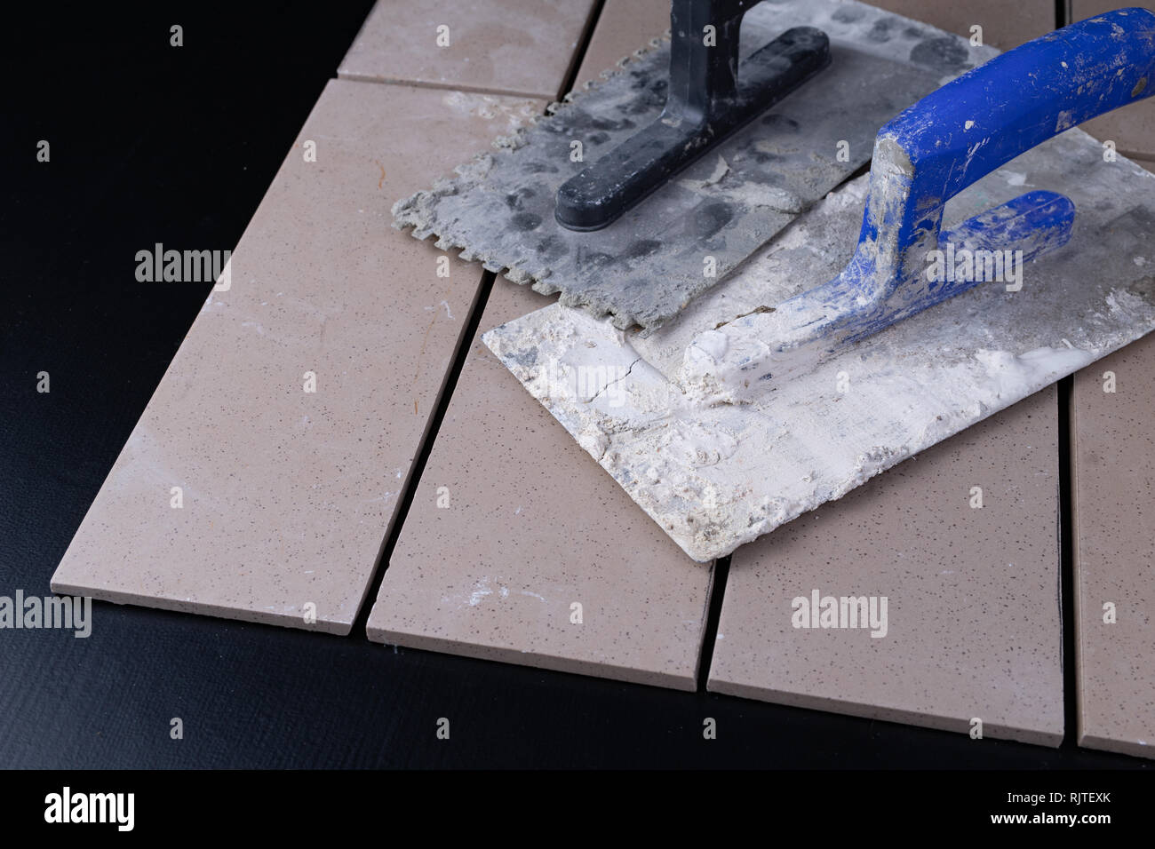 Tiles cut to size and trowels for applying mortar. Masonry accessories on a workshop table. Dark background. Stock Photo