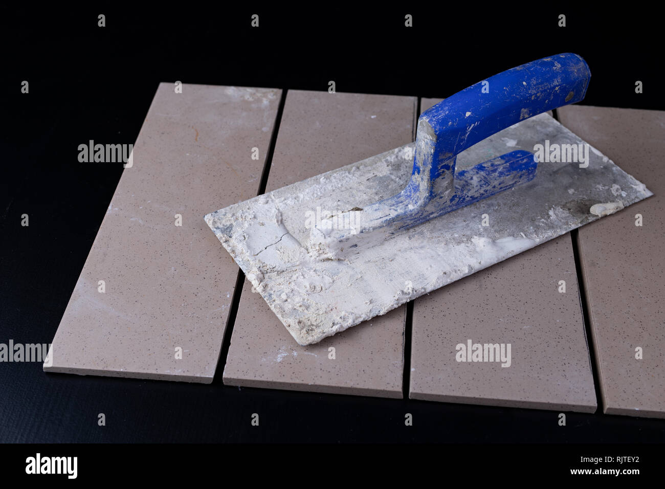Tiles cut to size and trowels for applying mortar. Masonry accessories on a workshop table. Dark background. Stock Photo