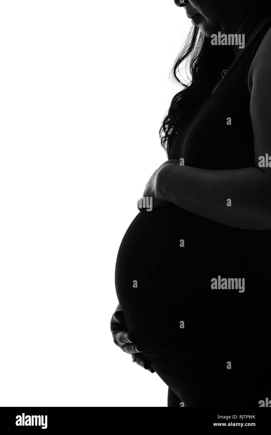 Silhouette of young mother with hands holding her pregnant tummy. Side profile view in black and white with copy space. Stock Photo
