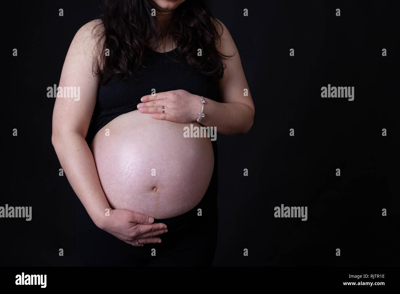 Young Asian pregnant mother with hands holding her baby in the tummy with copy space. Isolated on black background. Stock Photo
