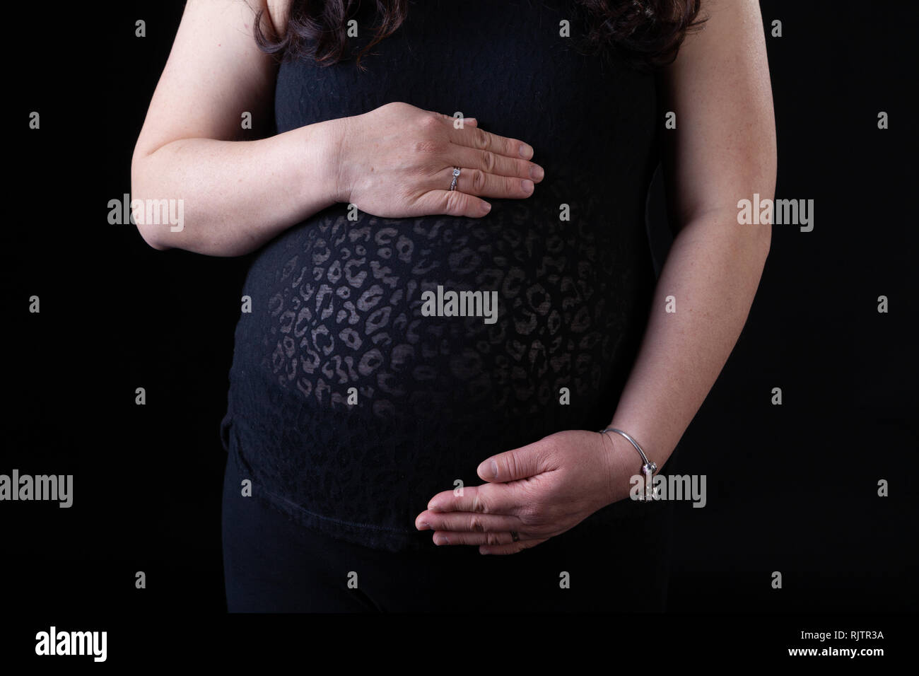 Young Asian pregnant mother with hands holding her baby in the tummy with copy space. Isolated on black background. Stock Photo