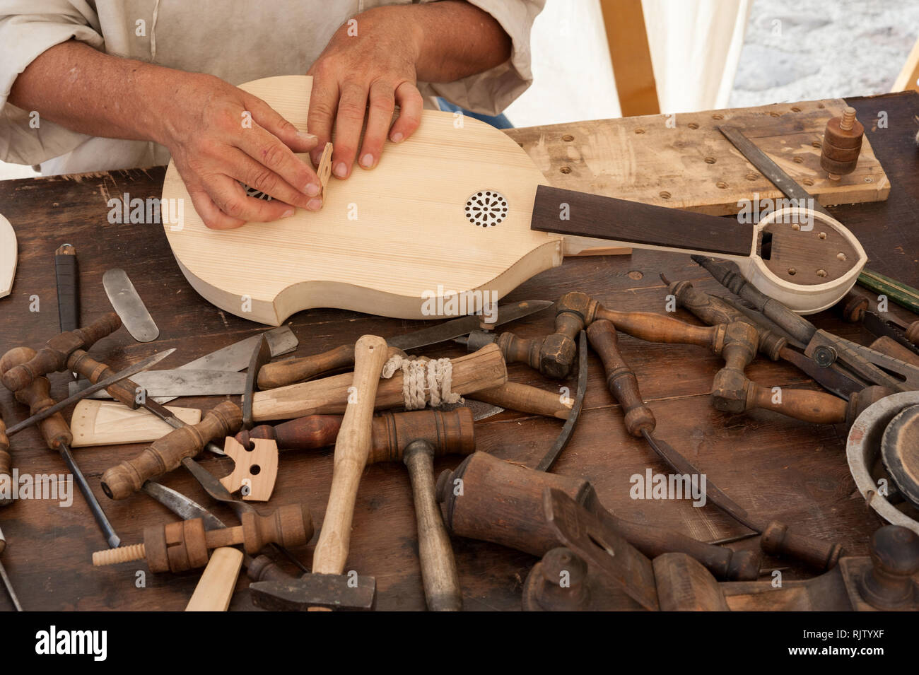 Luthier working on the creation of a stringed instrument. Various tools and instrument are placed on the workbench Stock Photo