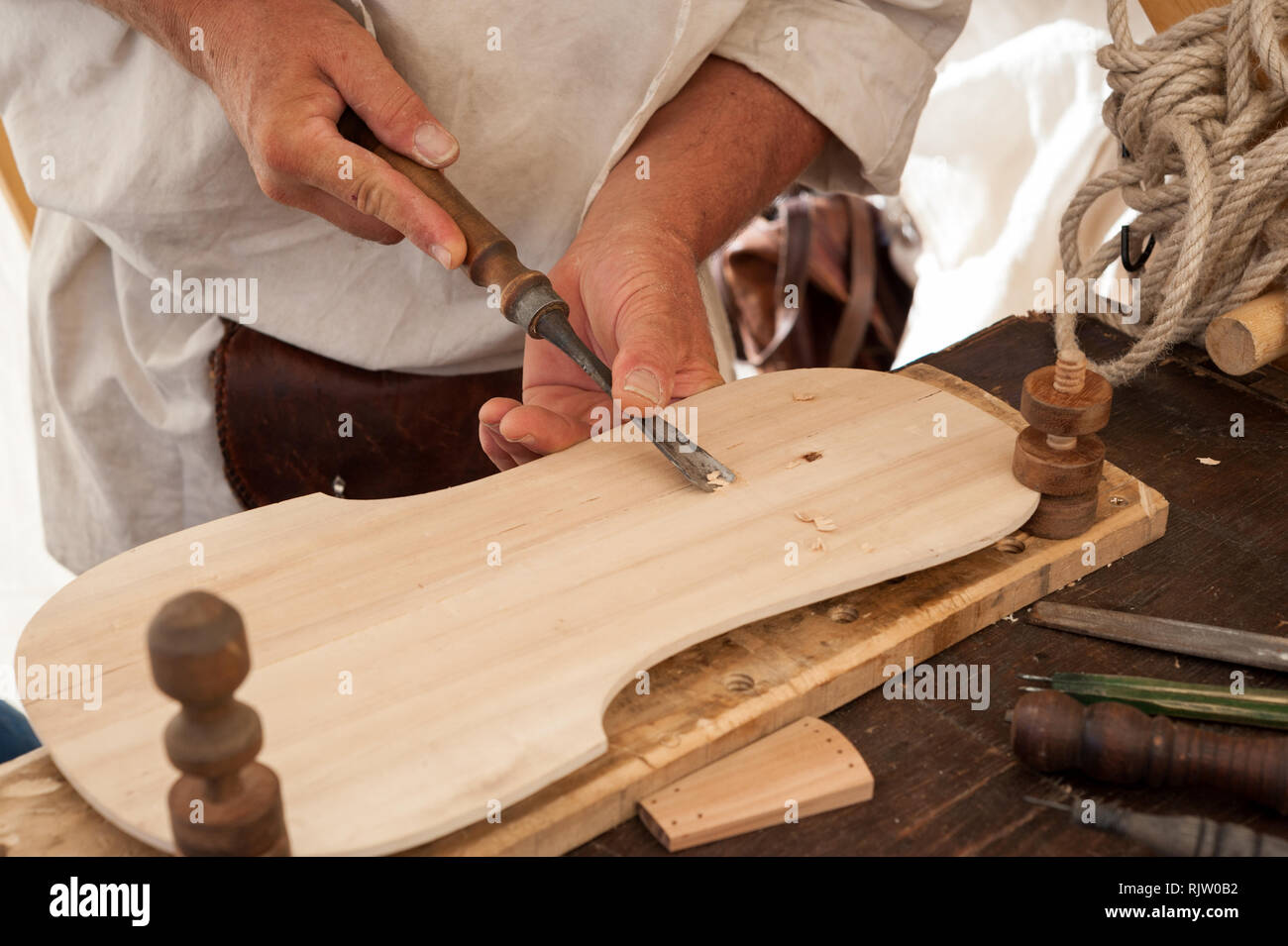 Luthier working on the creation of a stringed instrument. He uses a chisel to carve the top. Stock Photo