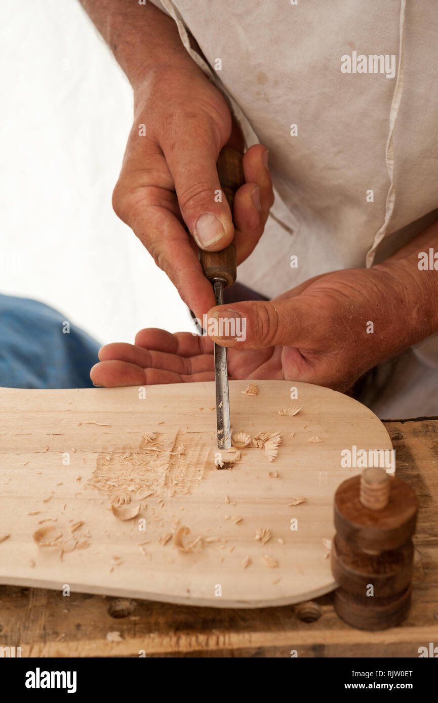 Luthier working on the creation of a stringed instrument. He uses a chisel to carve the top. Stock Photo
