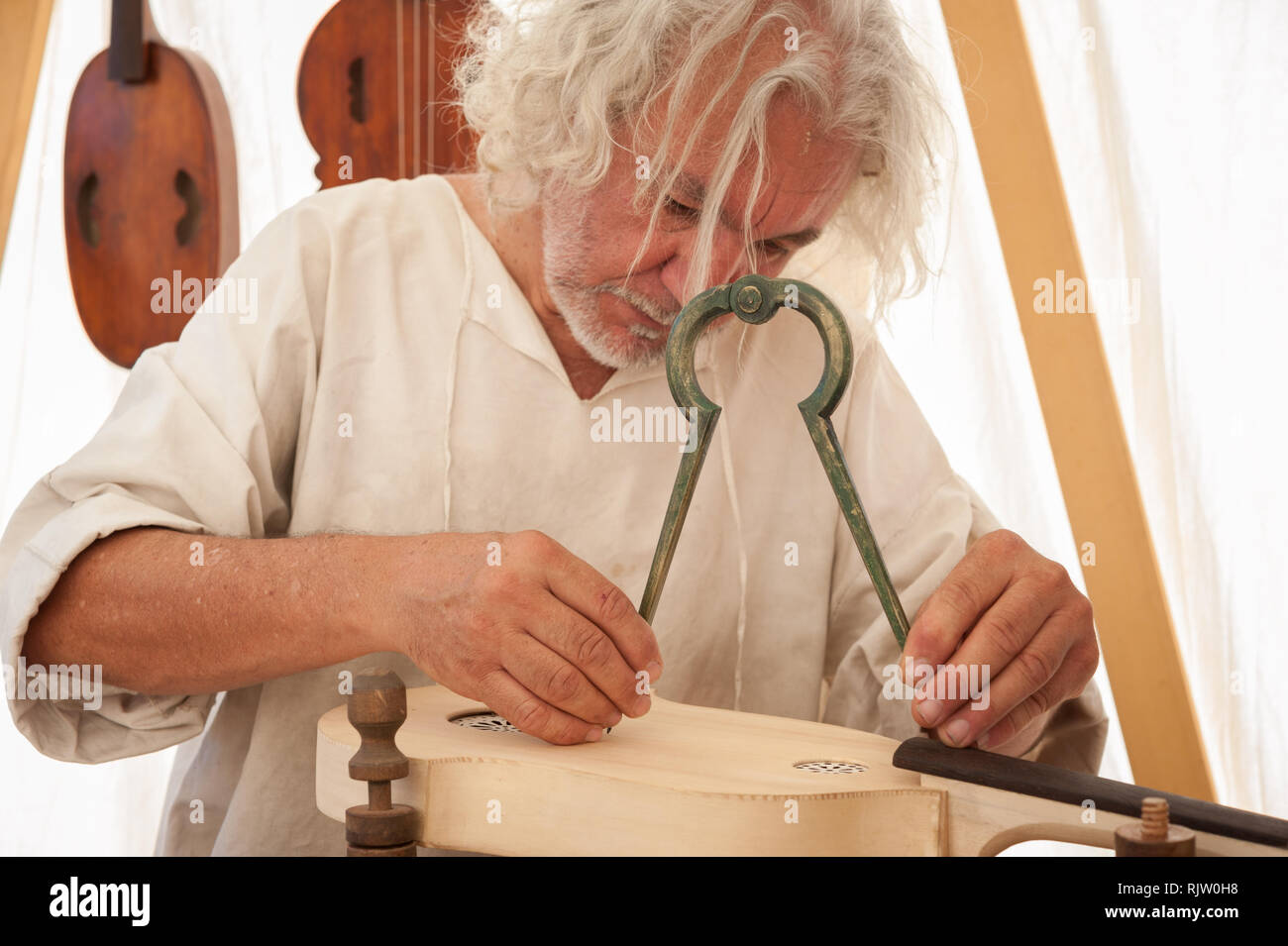 Luthier working on the creation of a stringed instrument. He uses a large compass to take the exact measure Stock Photo