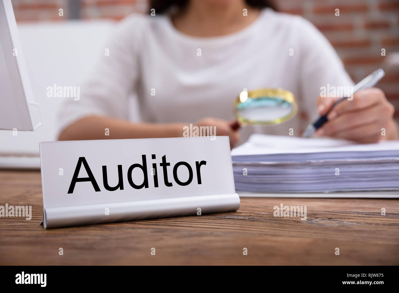 Nameplate With Auditor Title Kept On Desk In Front Of Businesswoman Examining The Invoices Stock Photo
