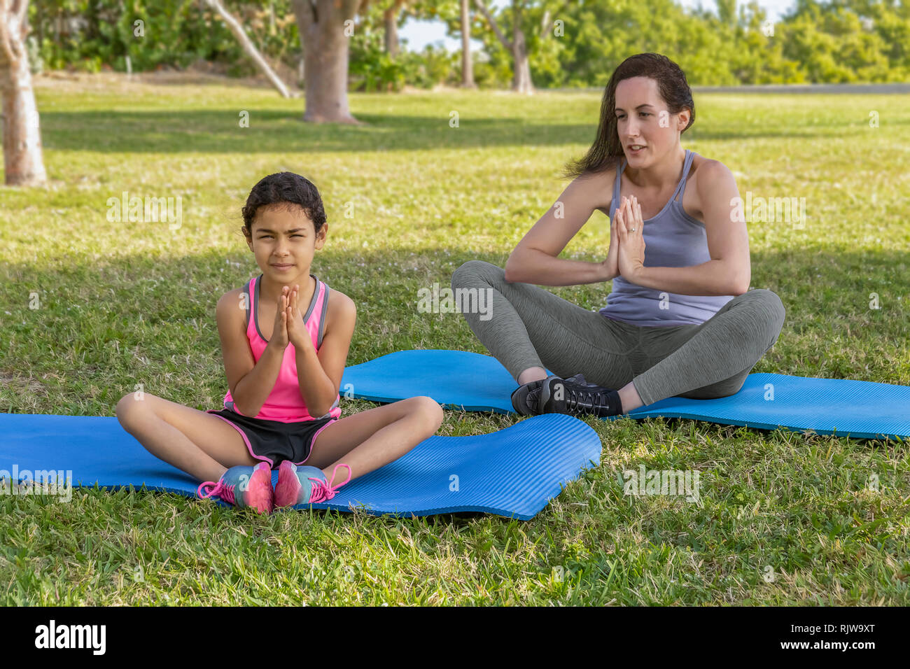 Mother and young daughter outside focused on yoga together.  A beautiful day at the park to enjoy family exercise. Stock Photo