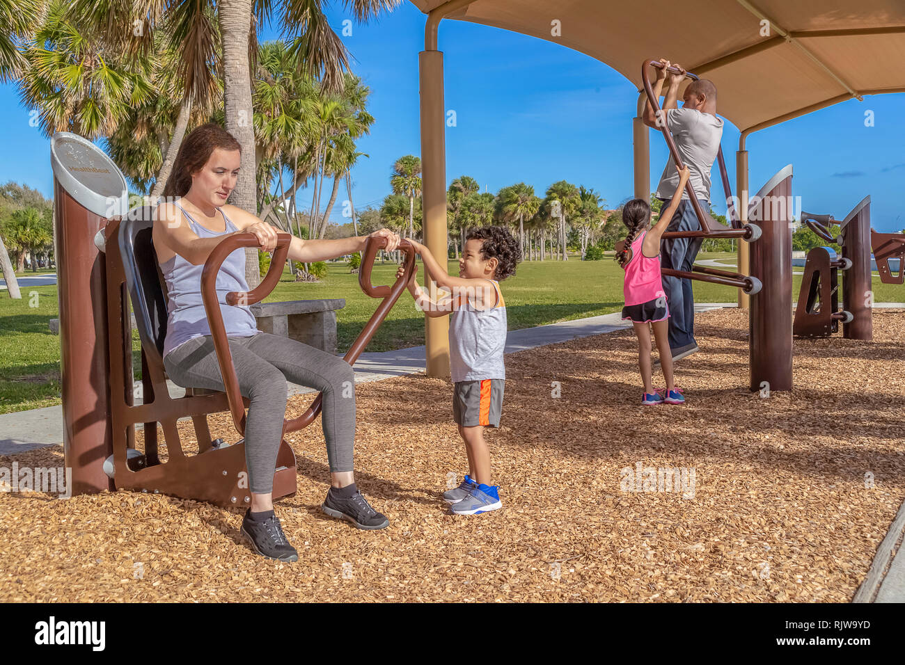 The modern family spends time at the outdoor gym working out together for better health. Teaching the kids healthy lifestyle habits at a young age. Stock Photo