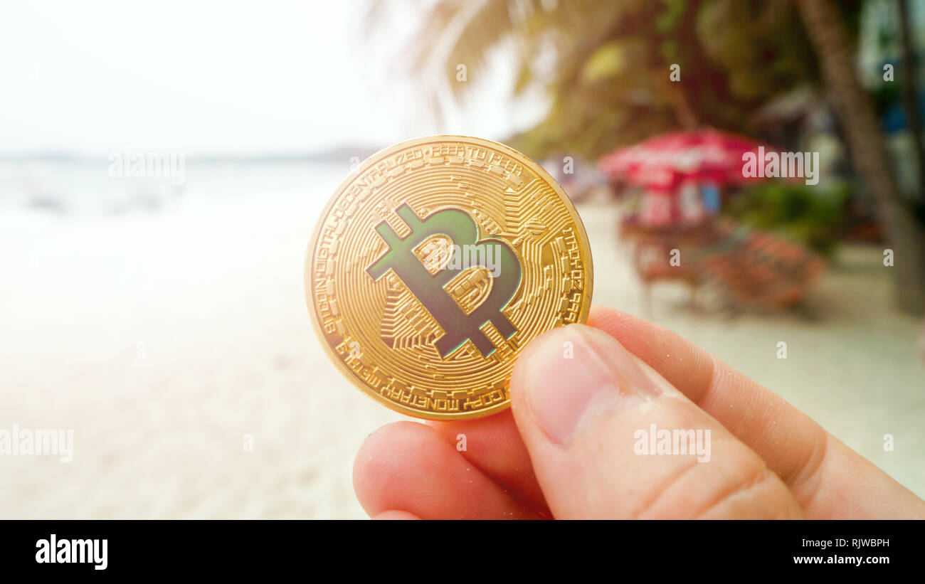 Hand holding golden bitcoin on the beach, on the background of sea wave.  Bitcoin is a modern way of exchange this crypto currency is a convenient  mean Stock Photo - Alamy
