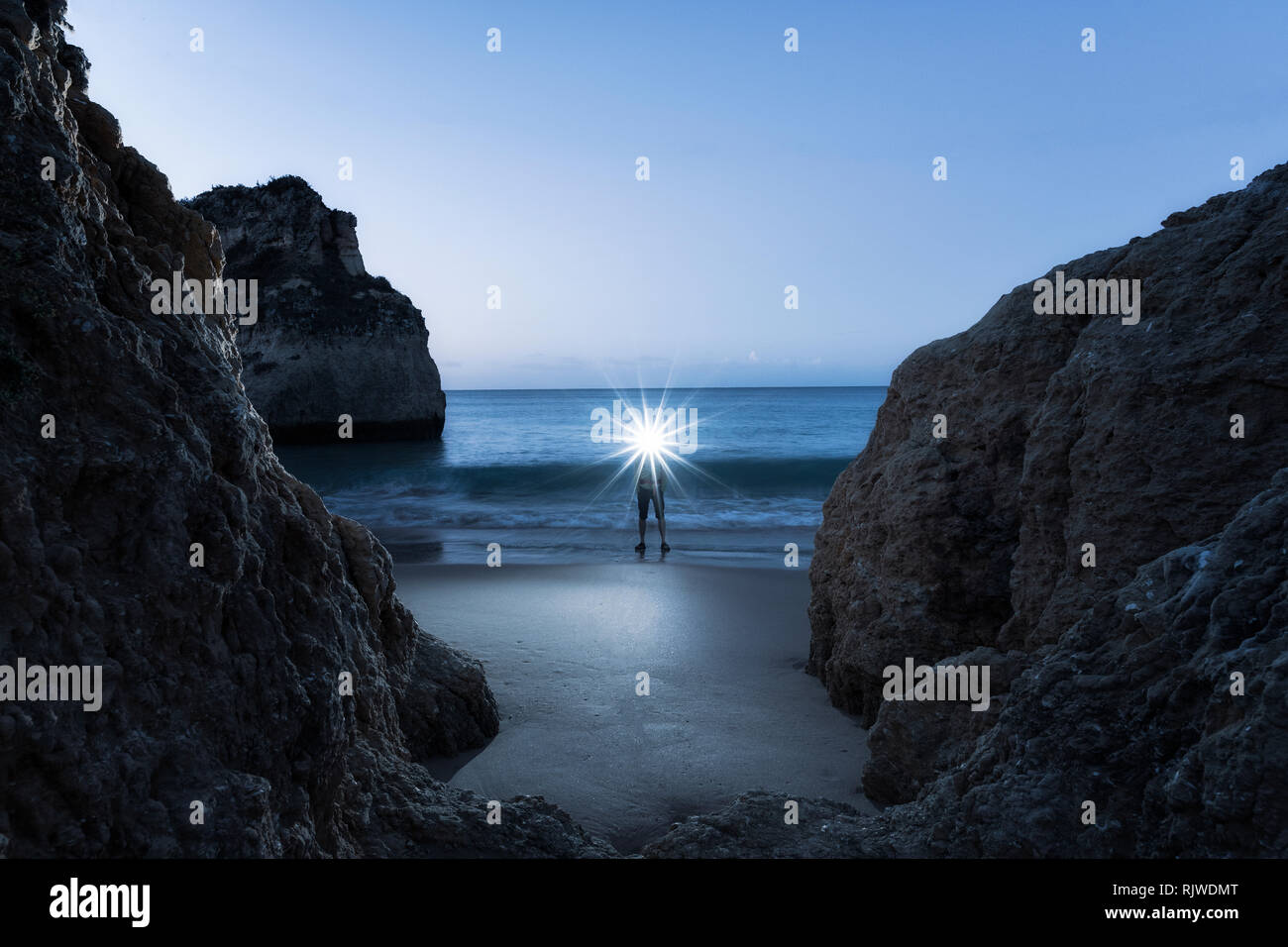 Man wearing illuminated headlamp, standing on beach by waters edge at sunset, Alvor, Algarve, Portugal, Europe Stock Photo