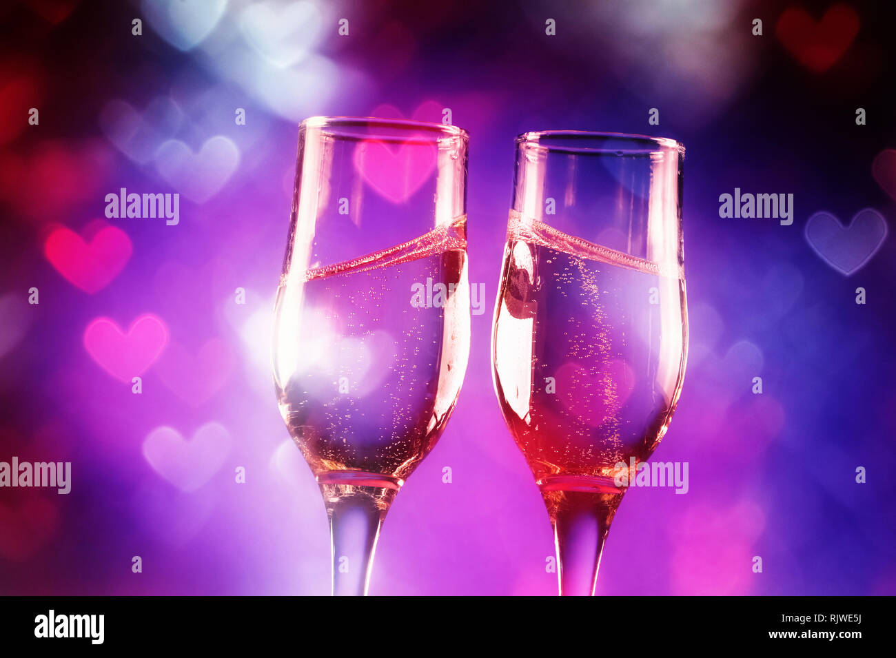 Two glasses of champagne with splash over heart shaped lights Stock