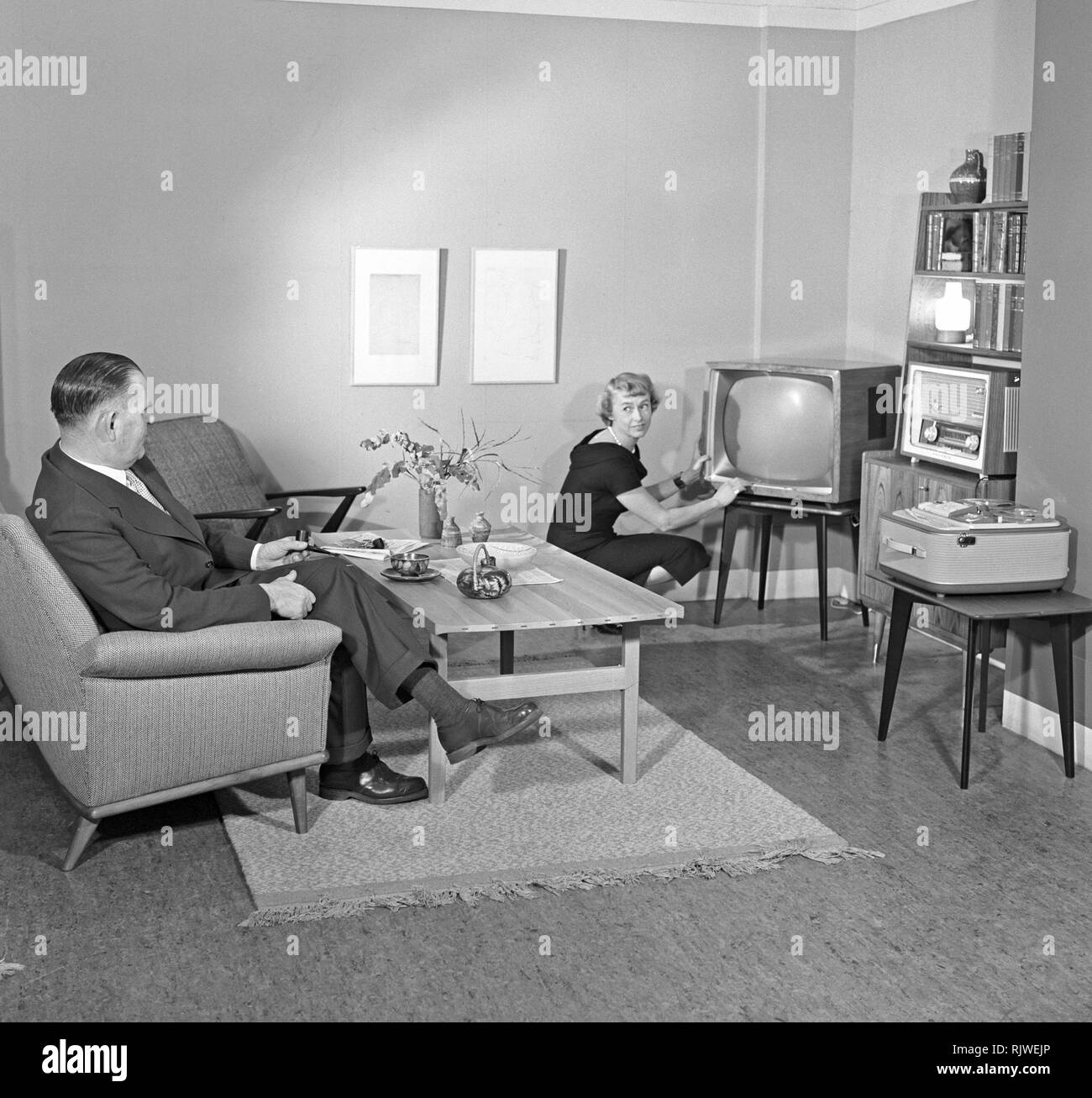 Television in the 1950s. A proud elderly man is pictured in his home with his wife with the latest in electronic home equipment visible. A typical television set on thin legs, a radio and a tape recorder.  Photo Kristoffersson ref CD88-10. Sweden 1959 Stock Photo