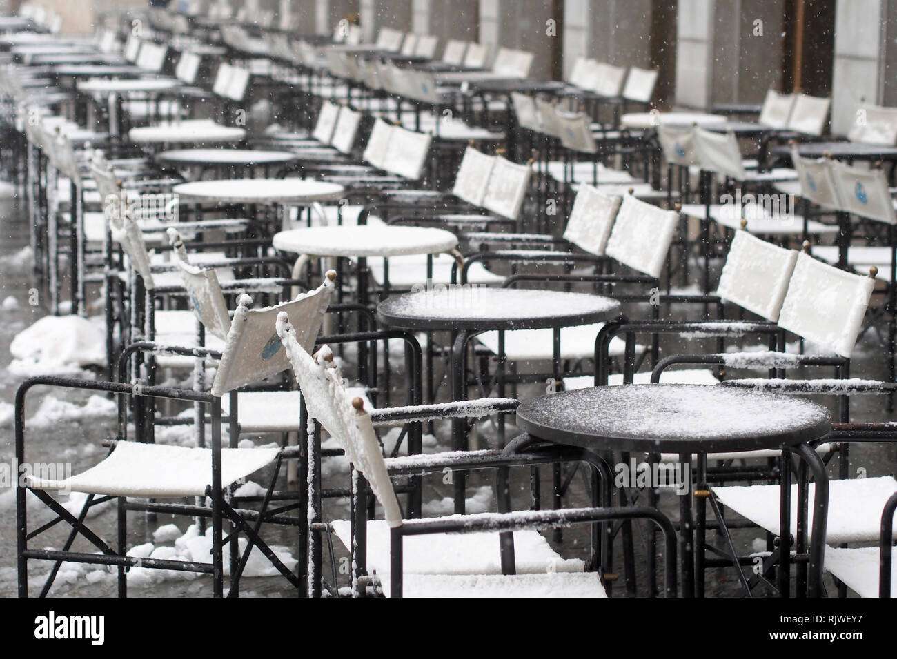 Seasonal concept image. Chairs and tables of a cafe bar covered with snow and ice. Stock Photo
