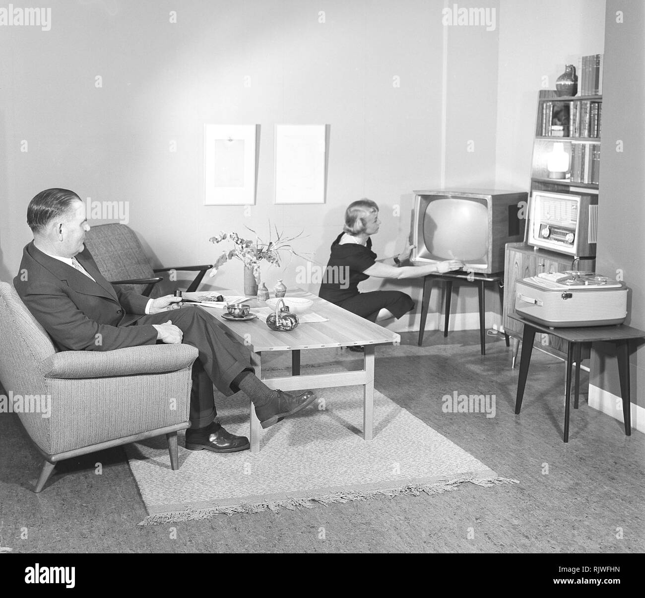Television in the 1950s. A proud elderly man is pictured in his home with his wife with the latest in electronic home equipment visible. A typical television set on thin legs, a radio and a tape recorder.  Photo Kristoffersson ref CD88-12. Sweden 1959 Stock Photo