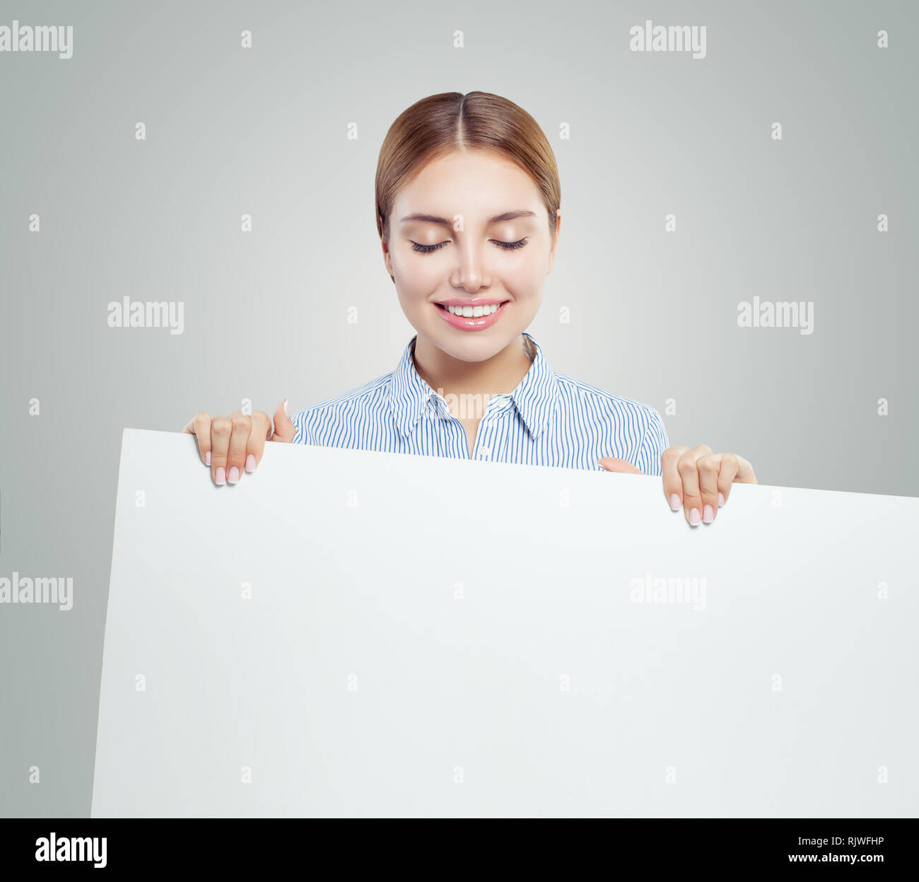 Young smiling woman showing white empty paper banner background with copy space. Happy woman portrait, business and education concept Stock Photo