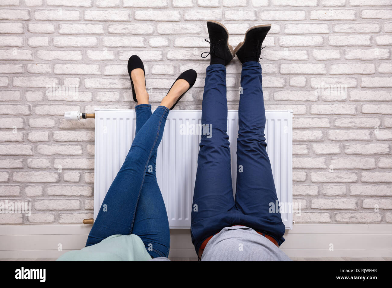 Close-up Of A Couple Warming Up Their Feet On White Radiator At Home Stock Photo
