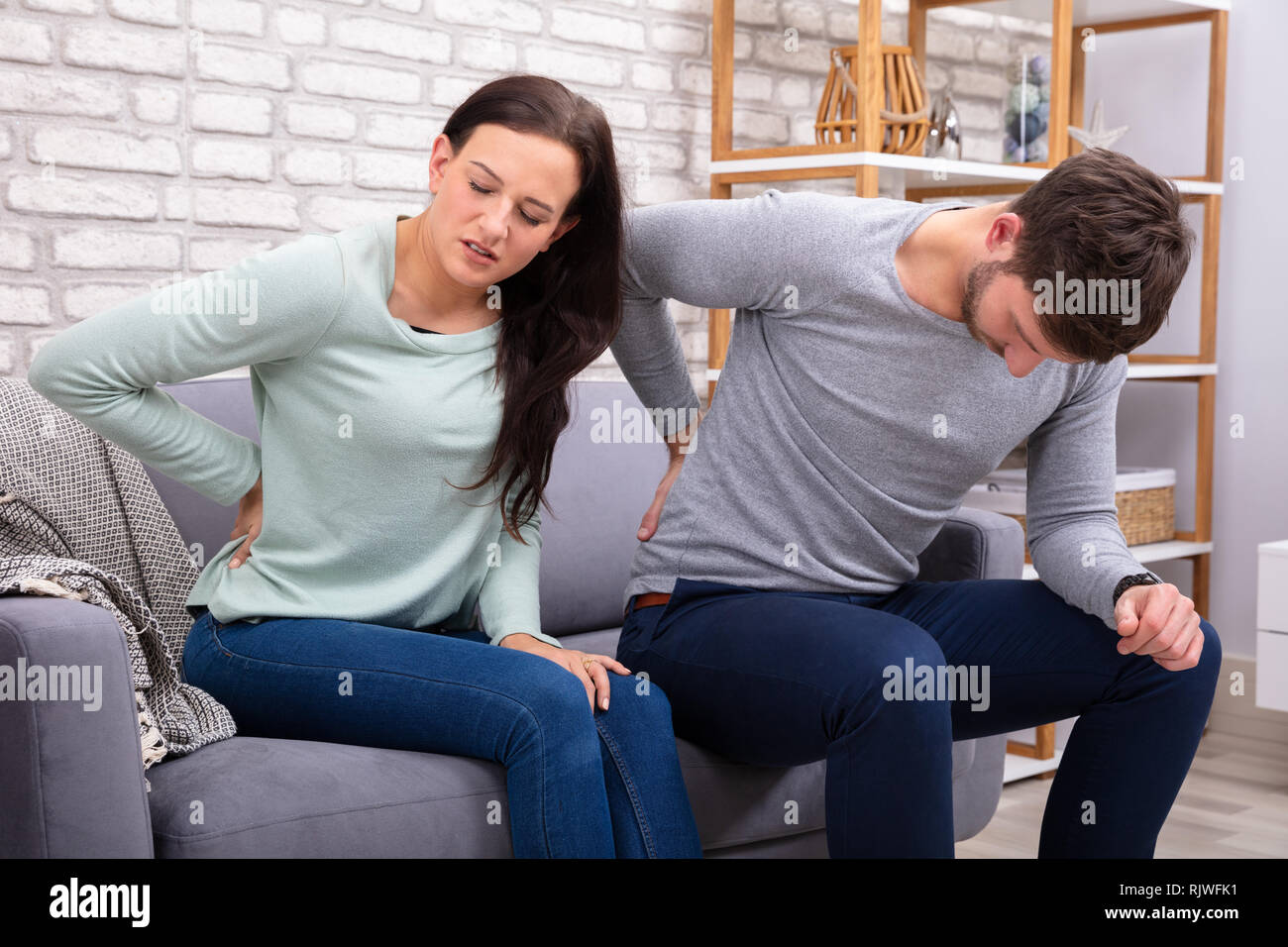 Sad Couple Sitting On Sofa Suffering From Backache Stock Photo
