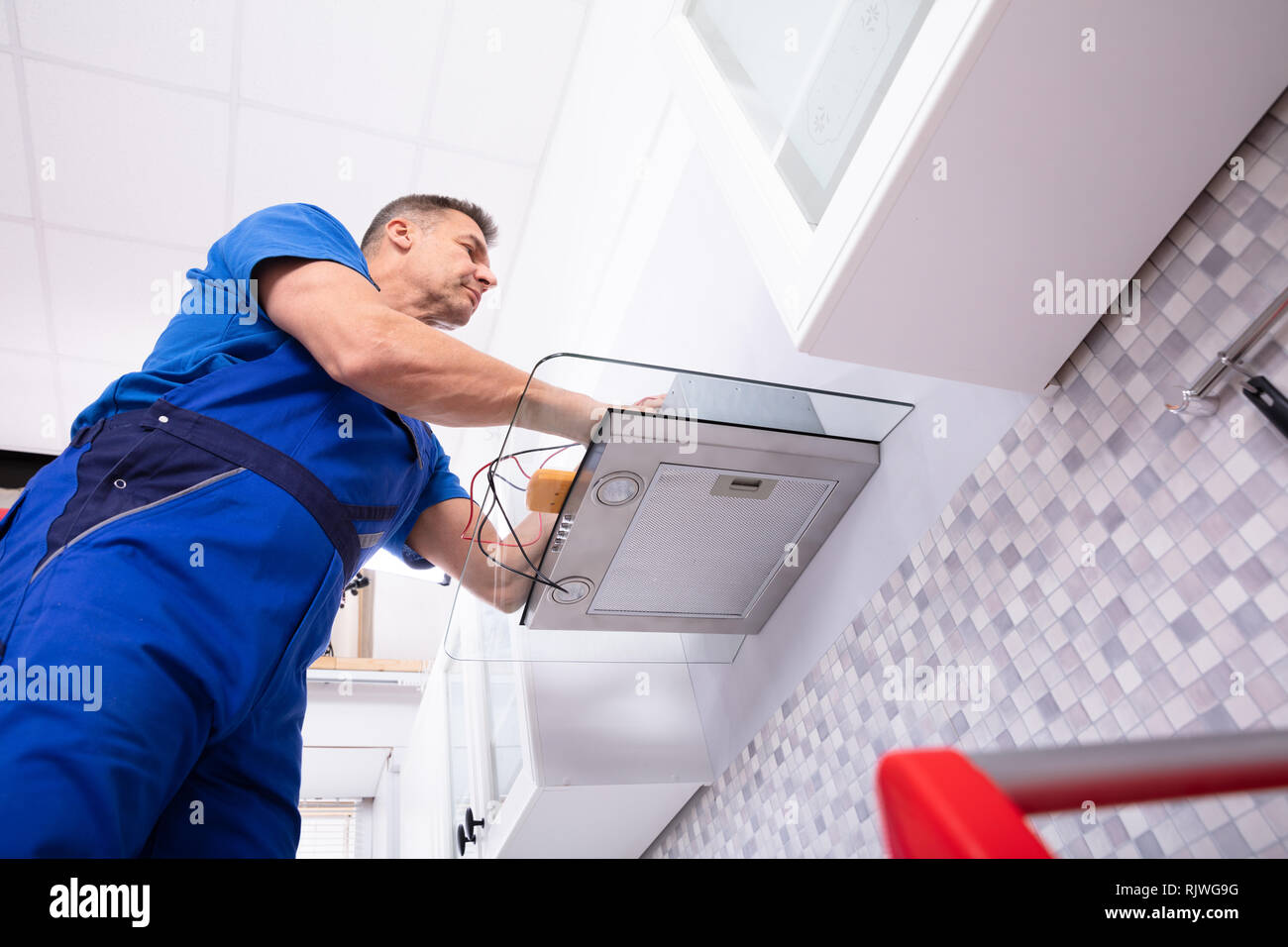 Elevated View Of Male Technician Checking Extractor Filter With Digital Multimeter In Kitchen Stock Photo