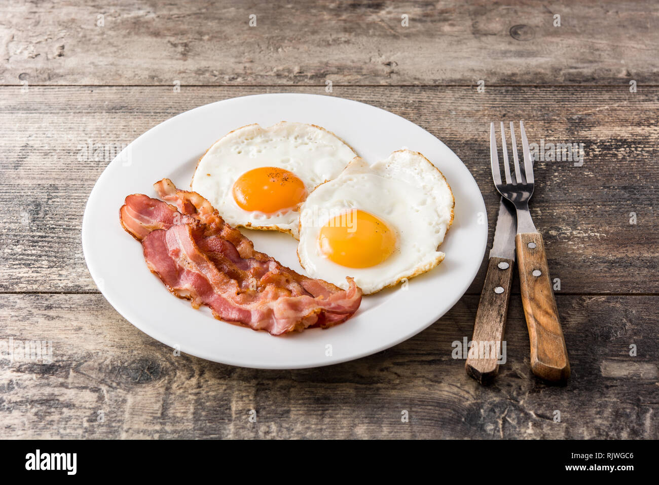 Fried eggs and bacon for breakfast on wooden table. Stock Photo
