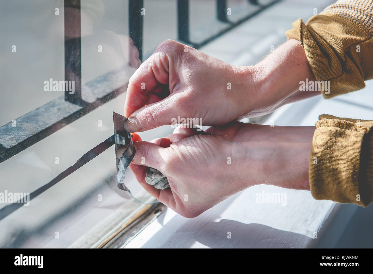 Hands of a woman using a razor blade to remove a decal from a store front window. Stock Photo