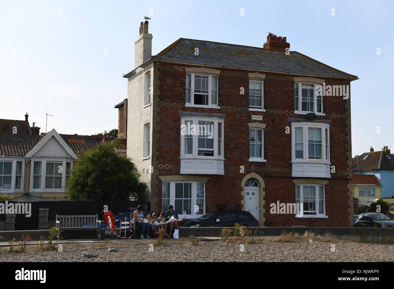 Victorian House situated on sea front with views out to sea.  Aldeburgh, Suffolk, England, UK. Young family eating fish and chips sitting on bench. Stock Photo
