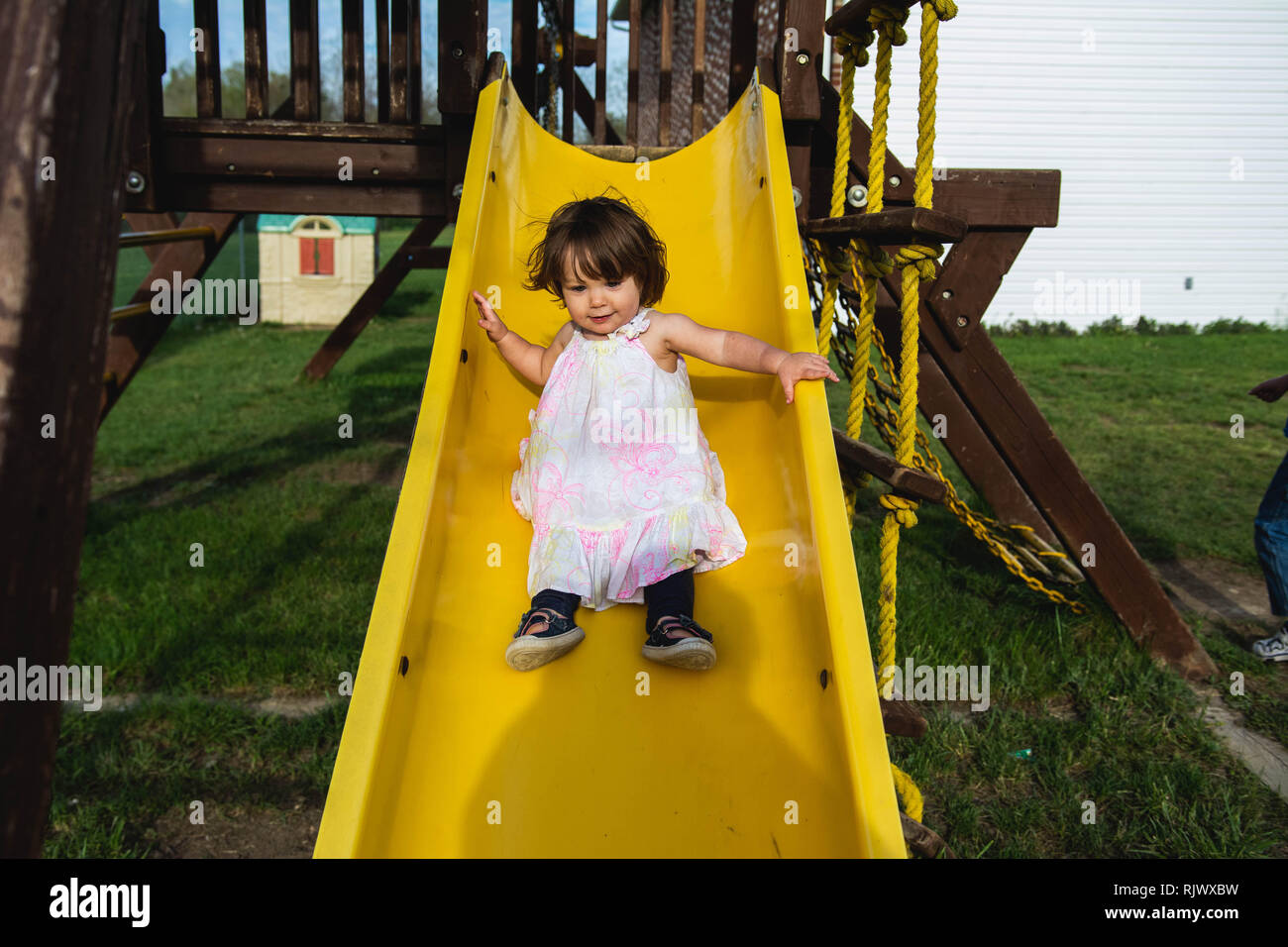 A 2 year old toddler girl slides down a slide at a playground during the summer. Stock Photo