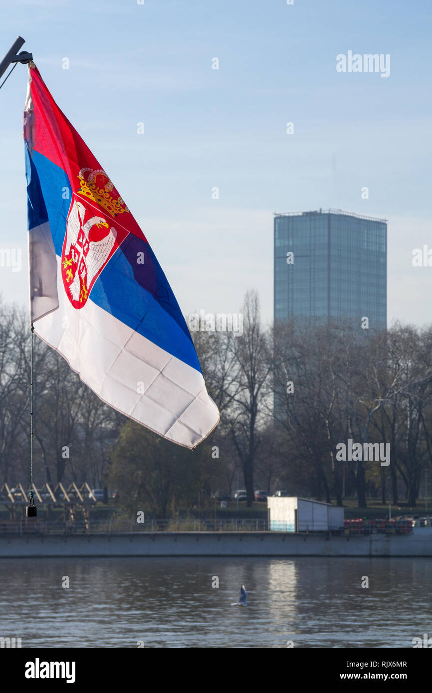 Photo of the official flag of the republic of Serbia, in front of a business building in Belgrade, Serbia, with a backround of blue sky and clouds  Pi Stock Photo