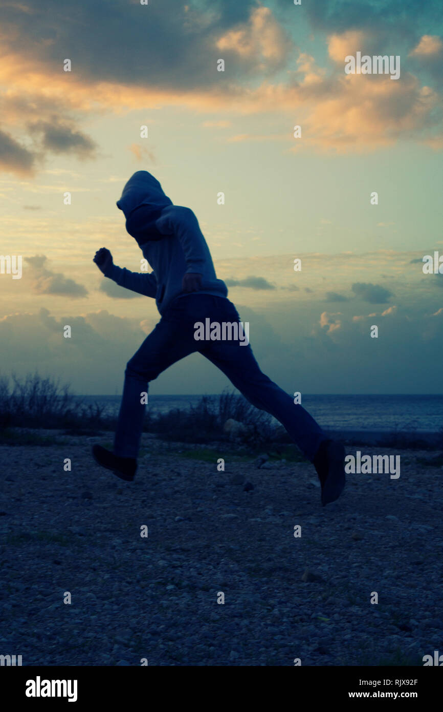 Mysterious hooded man running away at sunset Stock Photo