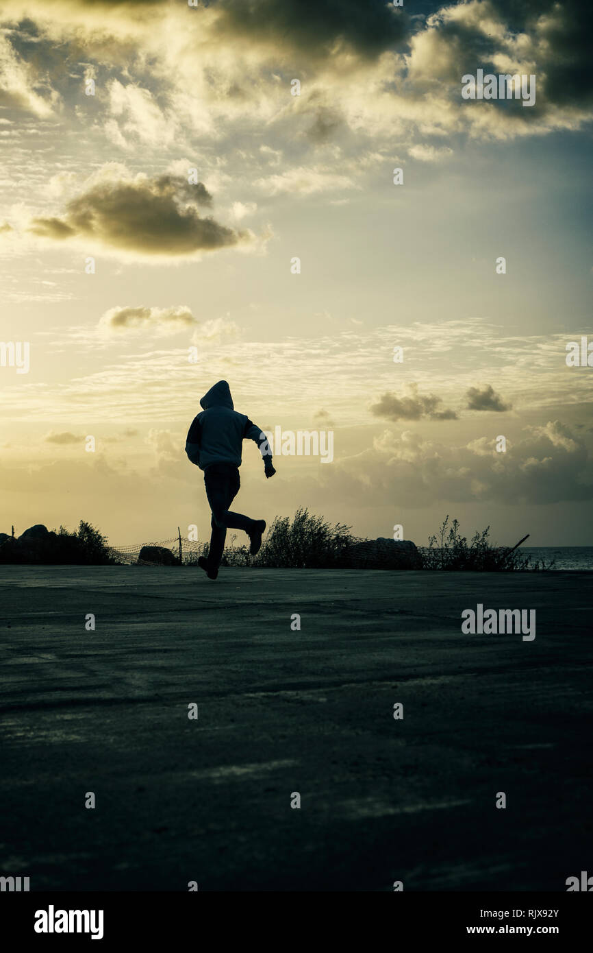 Mysterious hooded man running away at sunset Stock Photo