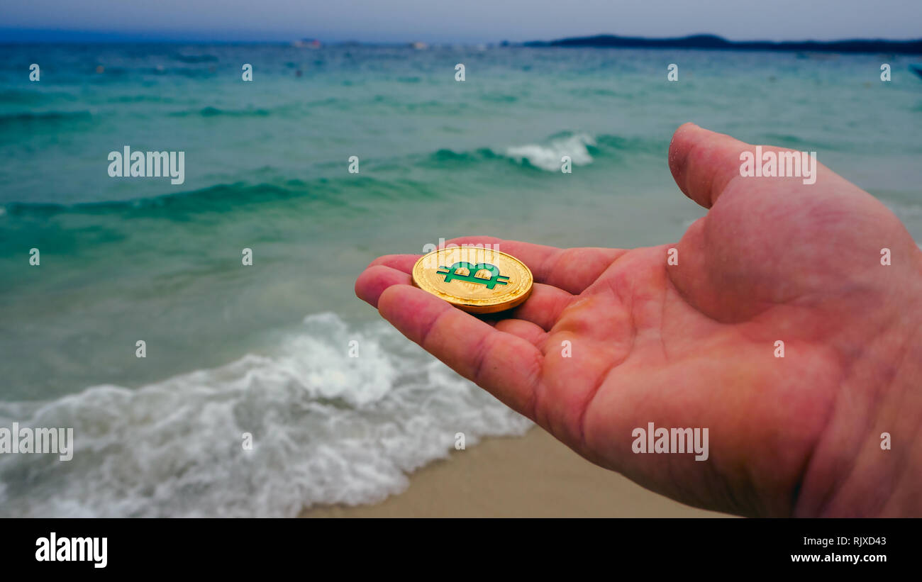 Hand holding golden bitcoin on the beach, on the background of sea wave.  Bitcoin is a modern way of exchange this crypto currency is a convenient  mean Stock Photo - Alamy