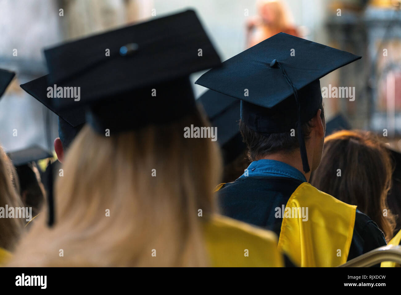 Students wearing gowns and hats sitting indoors, waiting to receive diplomas, graduation day in university, college commencement Stock Photo