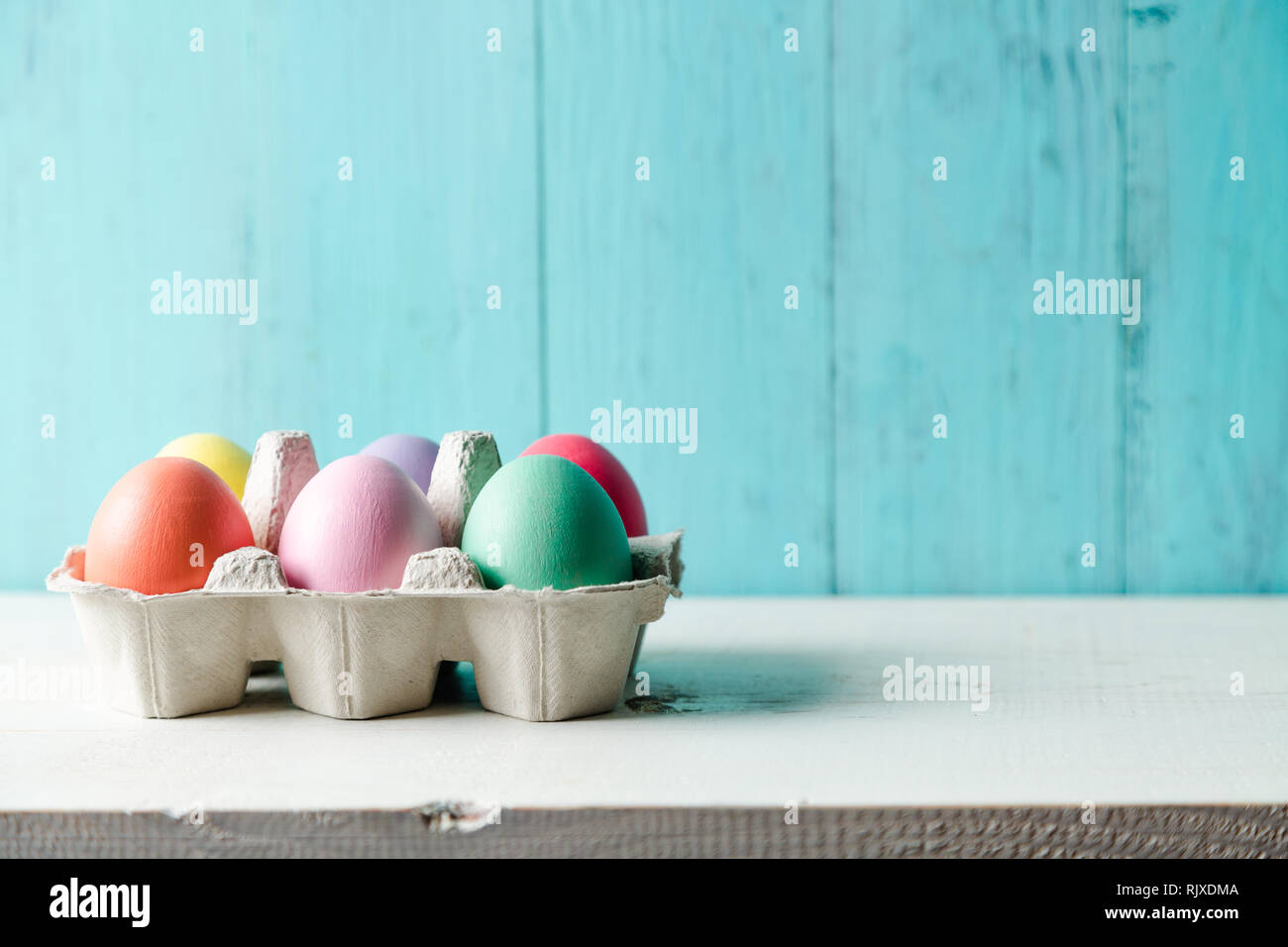 Pastel colored easter eggs in a egg box with a wooden turquoise background Stock Photo