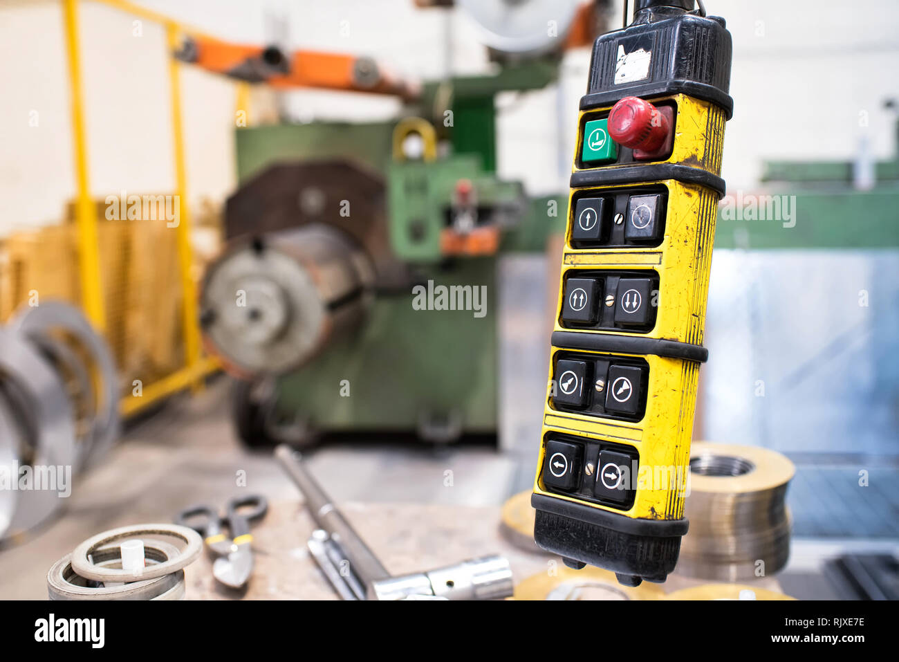 Crane remote control buttons in yellow case on wire. Lathe machine is blurred in background Stock Photo