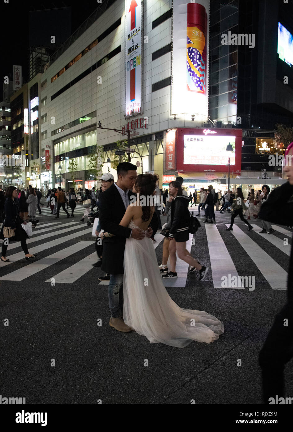 A bride in her wedding gown and groom kissing surrounded by crowds at ...