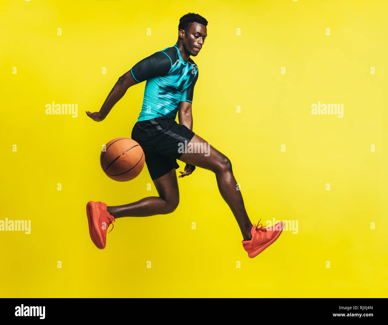 Young basketball player dribbling a ball over yellow background. Man in sportswear practicing basketball. Stock Photo