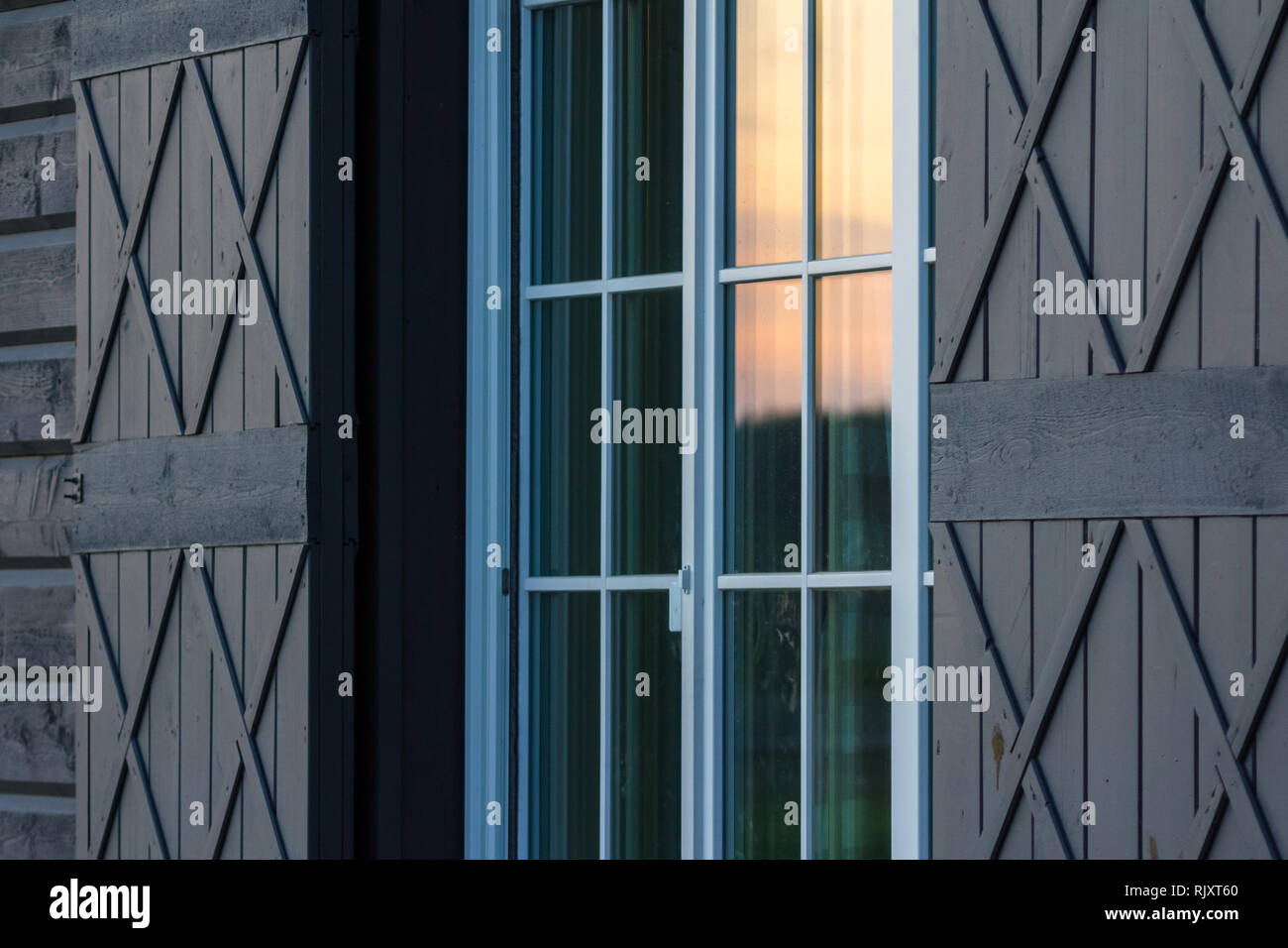 Detail of wooden home exterior. Warm evening light reflection on glass windows. Stock Photo