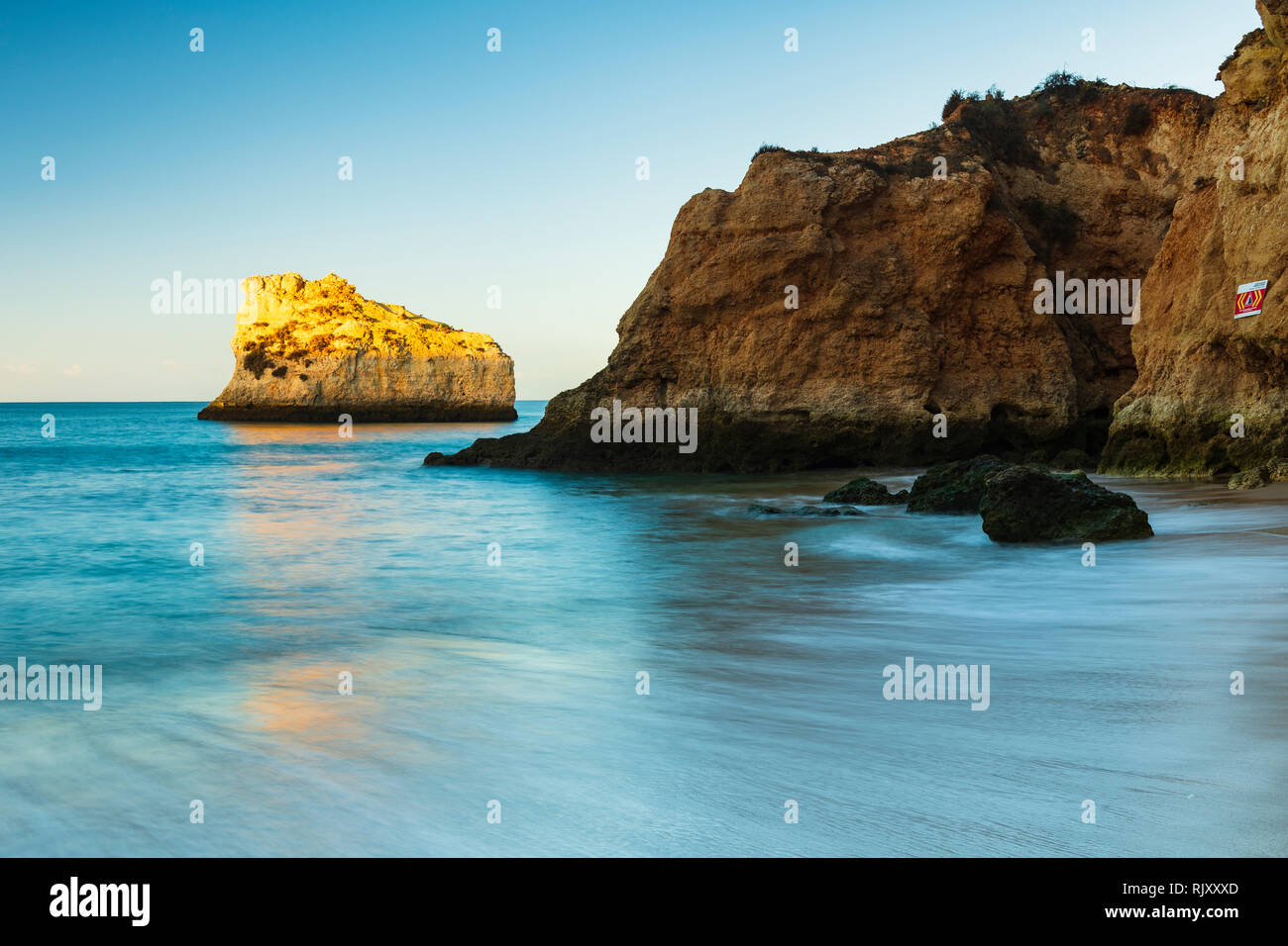 View from sandy beach of sunlight illuminating rock formation, Alvor, Algarve, Portugal, Europe Stock Photo