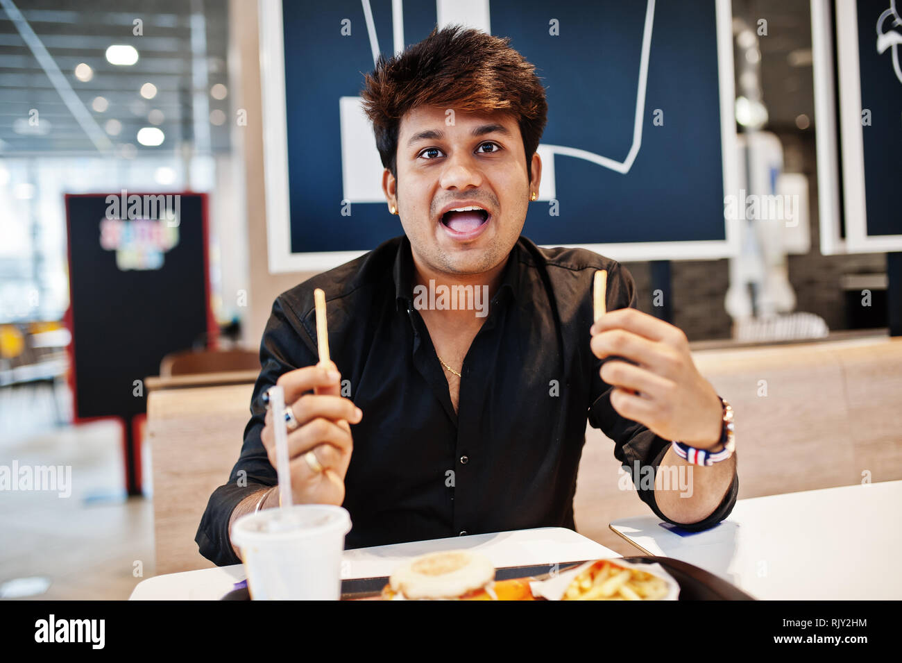 Funny and stylish indian man sitting at fast food cafe and eating french fries, show his tongue Stock Photo - Alamy Funny and stylish indian man sitting at fast food cafe and eating french fries, show his tongue Stock Photo - Alamy
