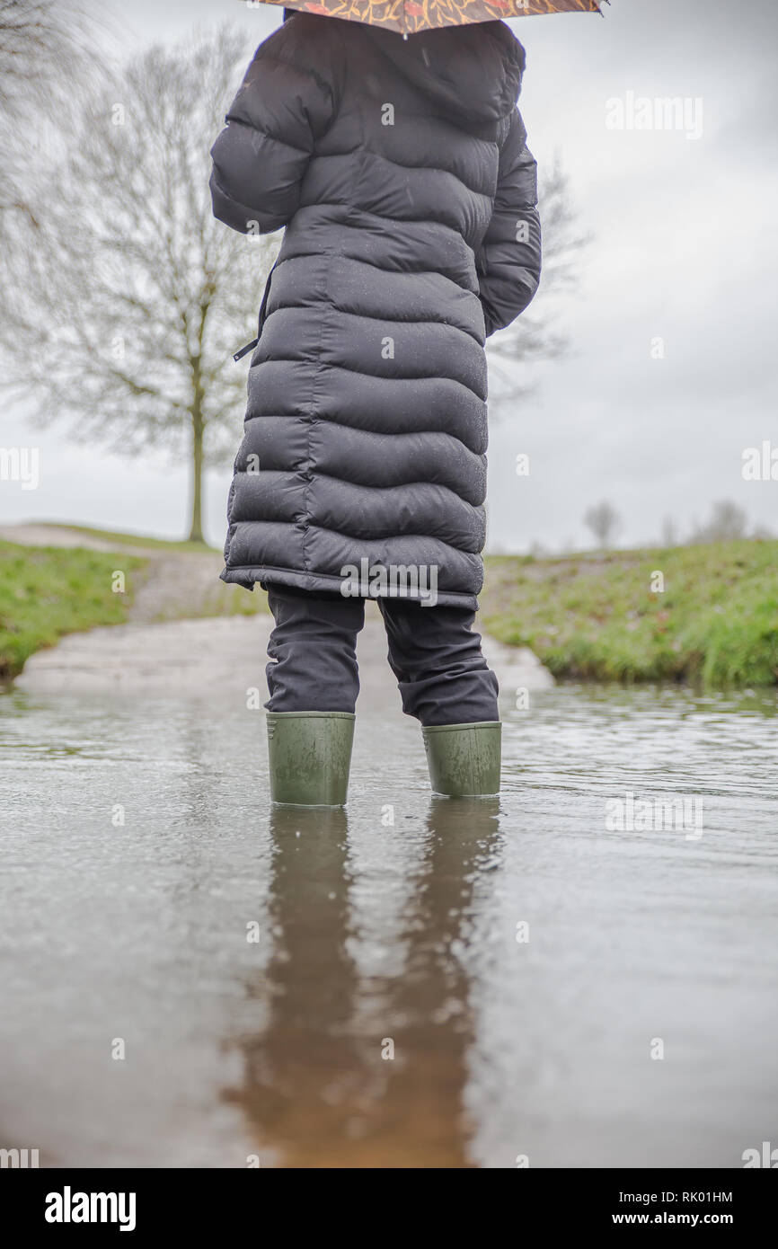 Kidderminster, UK. 8th February, 2019. UK weather: persistent heavy rain leads to water levels rising in Worcestershire with blustery showers continuing throughout the day. A young lady, rear view, wearing long, winter coat and wellies is standing isolated outdoors in winter flood water. Credit: Lee Hudson/Alamy Live News Stock Photo
