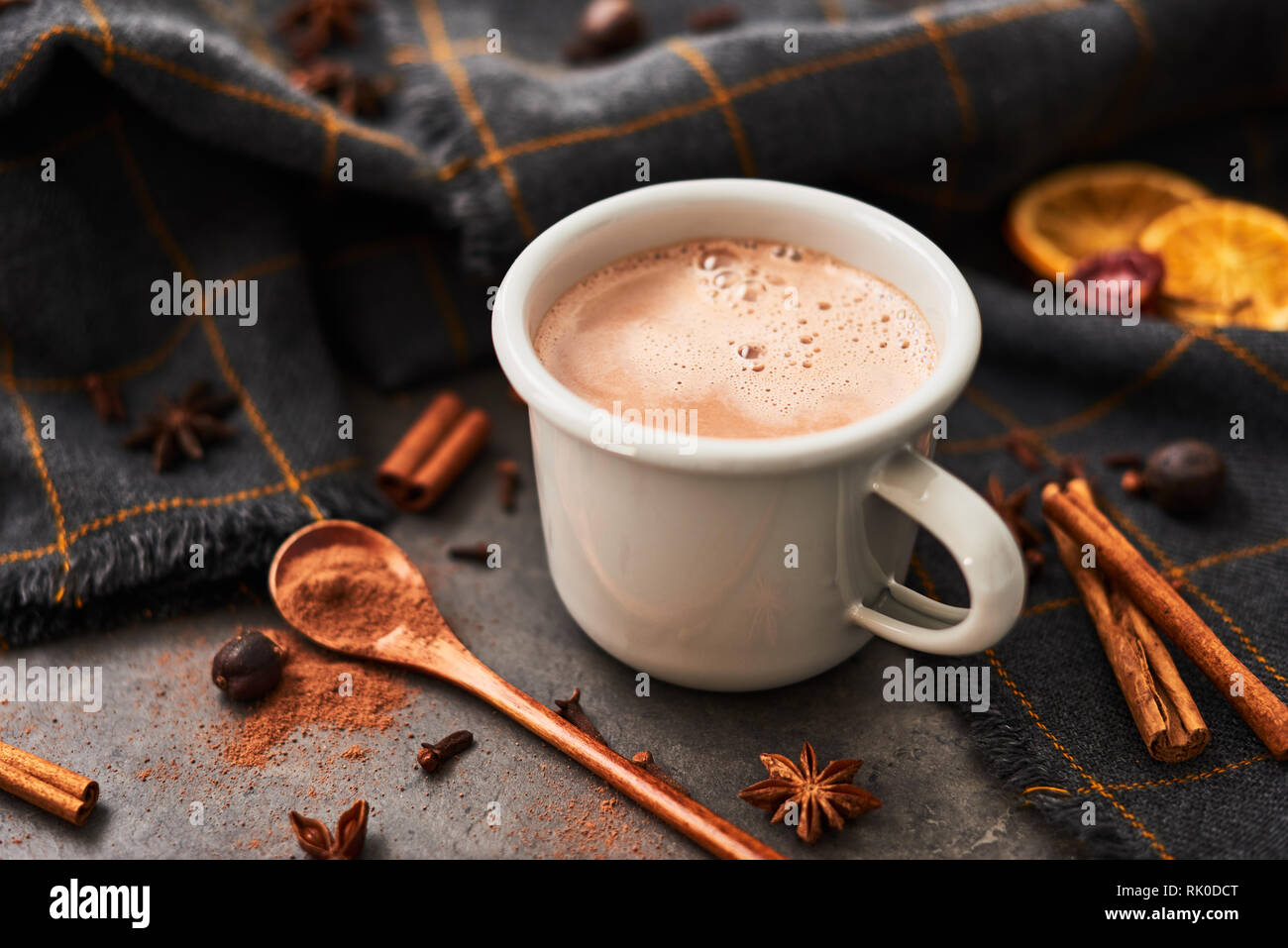 Hot cocoa drink in retro mug with ingredients: cinnamon, orange, anise and cove on black concrete table. Winter drink. Rustic look. Copy space for tex Stock Photo