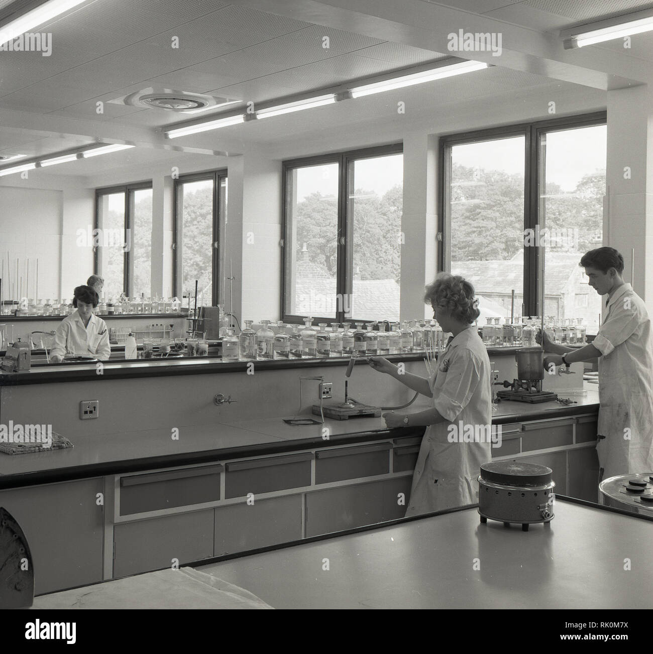 1960s, young adult scientific technicians in white-coats working in a light, modern laboratory. Such workers are the backbone of scientific research and investigation as their job entials collecting, preparing and testing samples. Stock Photo