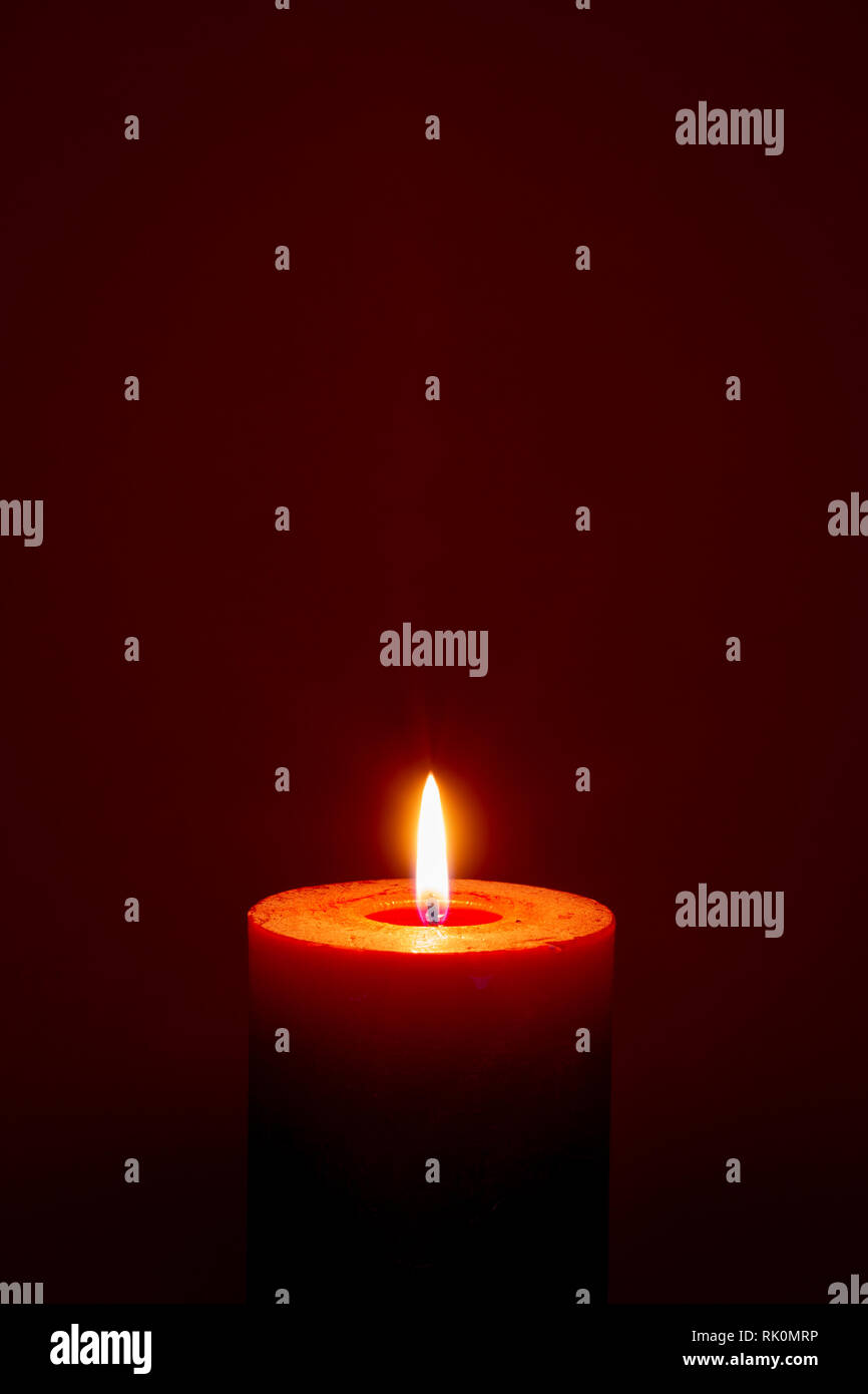 Single burning red candle on dark red background closeup Stock Photo